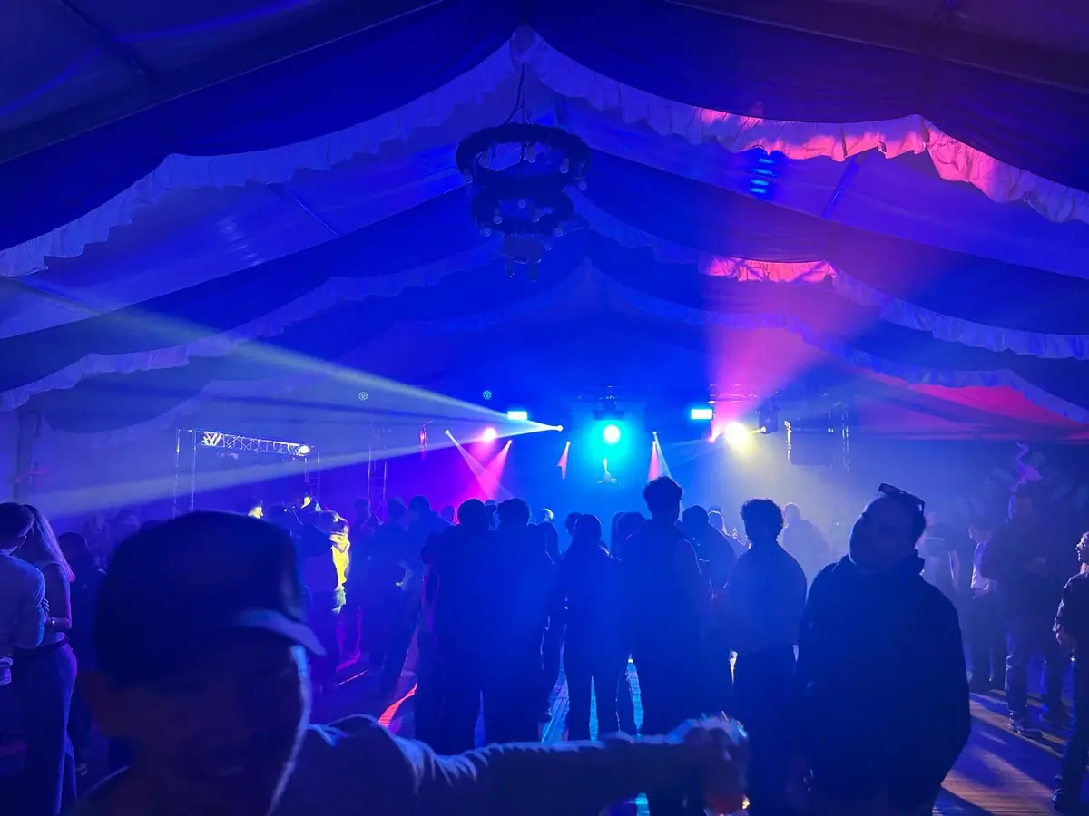Tanzfläche in einem Festzelt mit blauem und violettem Licht und Lichtstrahlen vom DJ-Platz