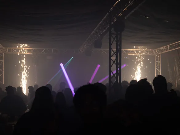 Silhouetten von Gästen vor violetten Lichtstrahlen und Funkenfontänen unter Traversen